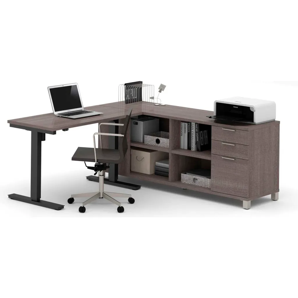A sit-stand desk with a laptop on it and a printer on a credenza and a chair