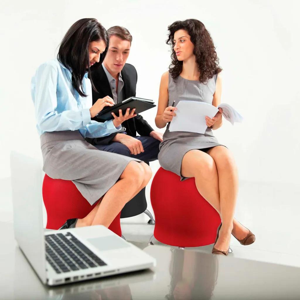Three people sitting on red, egg-shaped chairs with silver bases, engaged in a meeting.