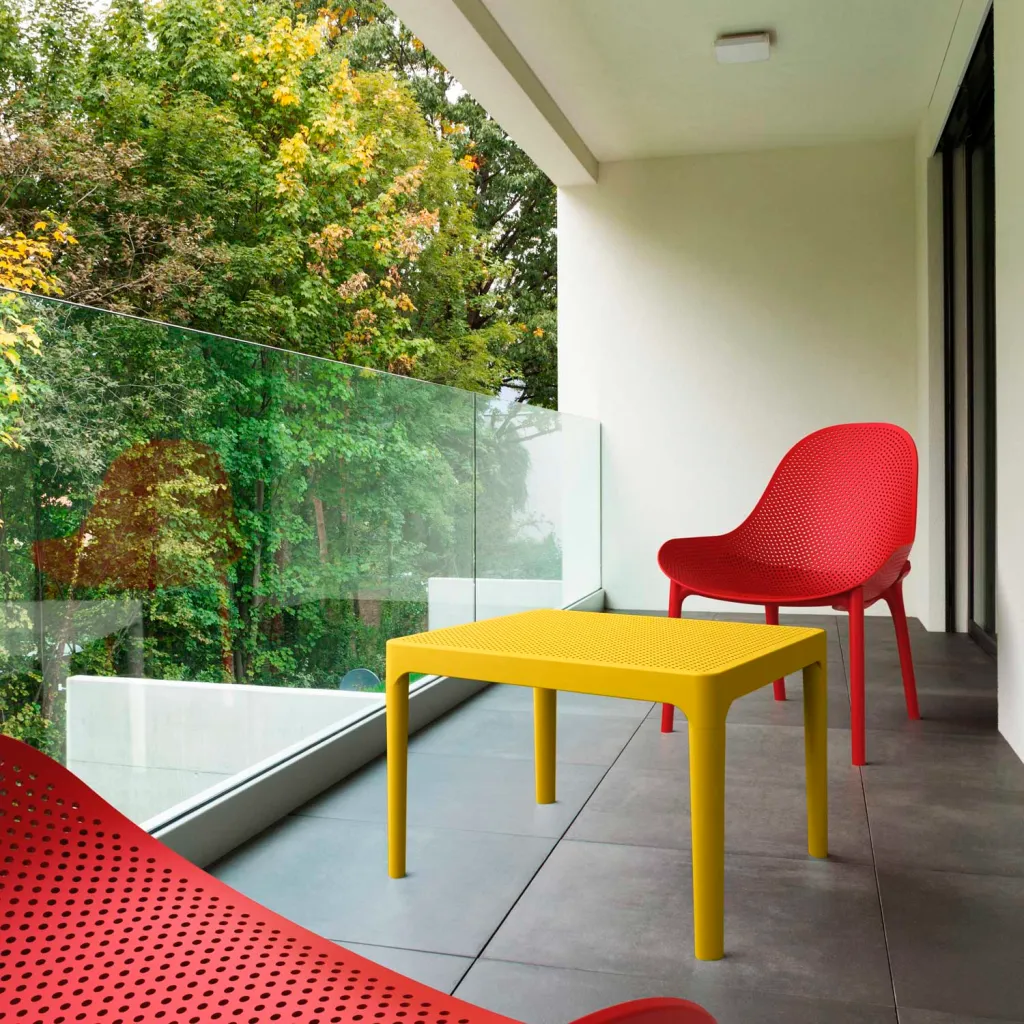 Yellow plastic table on balcony with red chair and trees in background