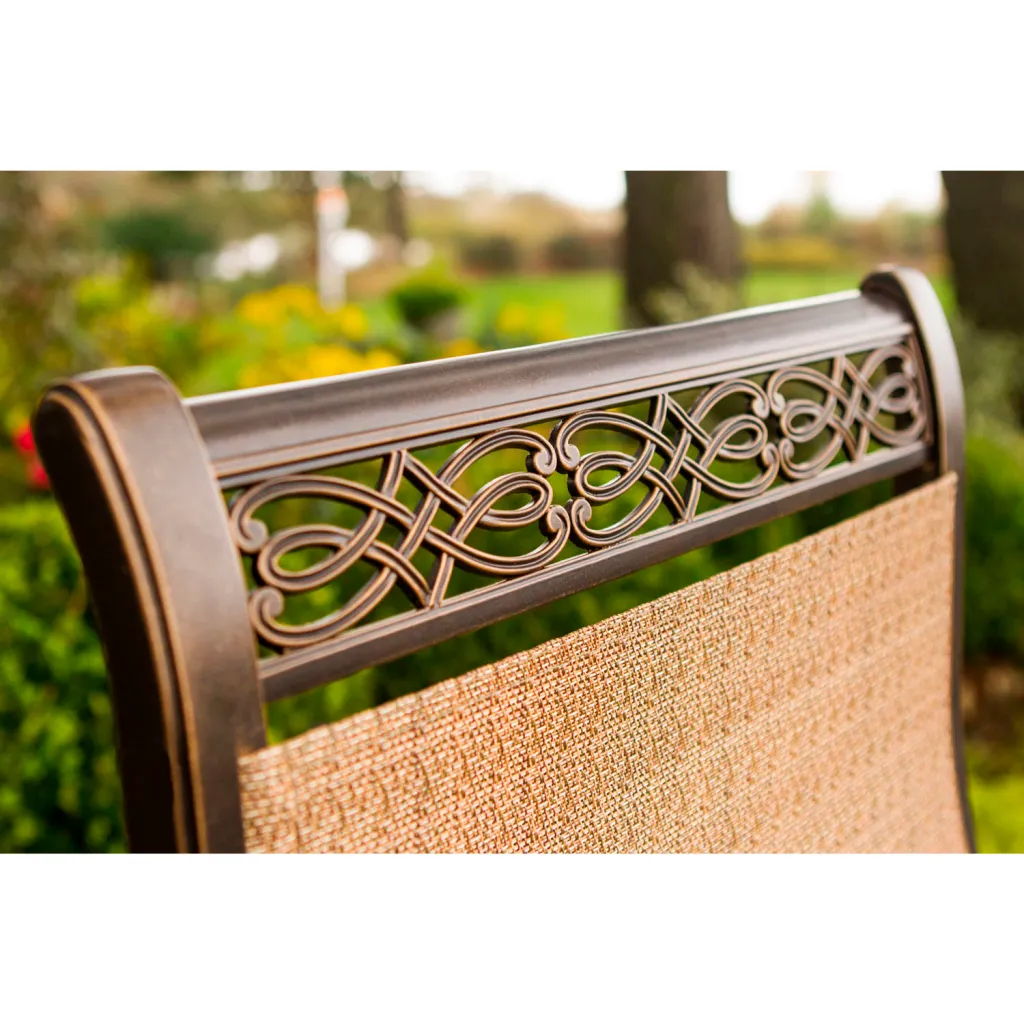 Close-up of bronze-finished metal chair backrest with intricate design and tan fabric.
