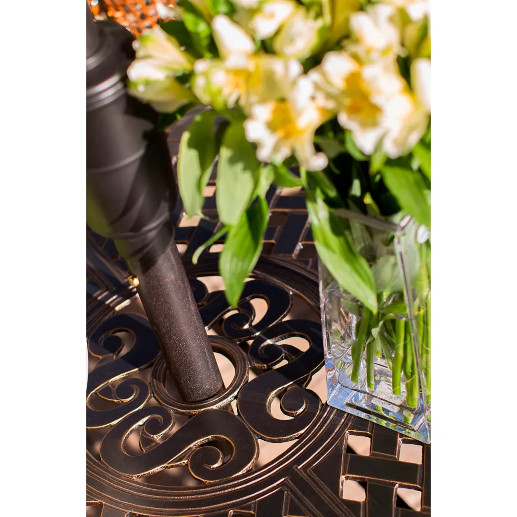 Close-up of bronze-finished metal table with intricate design and vase of flowers.