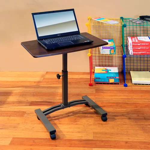 A rolling laptop stand with a laptop on it, next to a bookshelf
